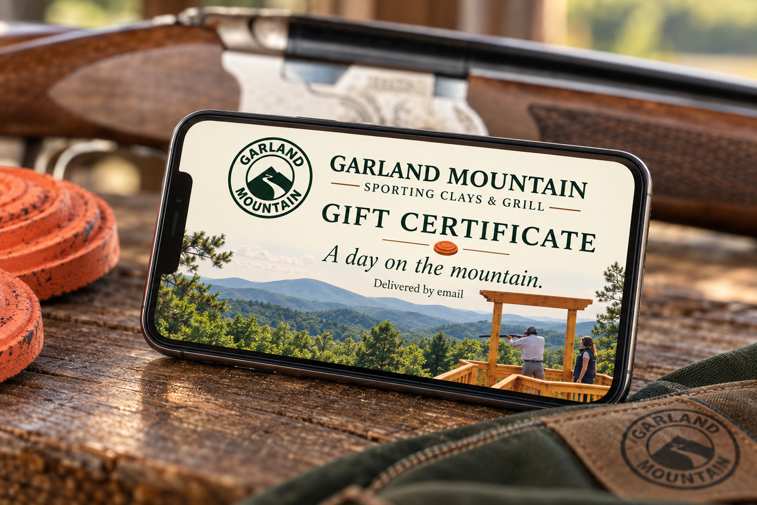 Garland Mountain digital gift certificate displayed on a phone beside clay targets on a rustic wooden table
